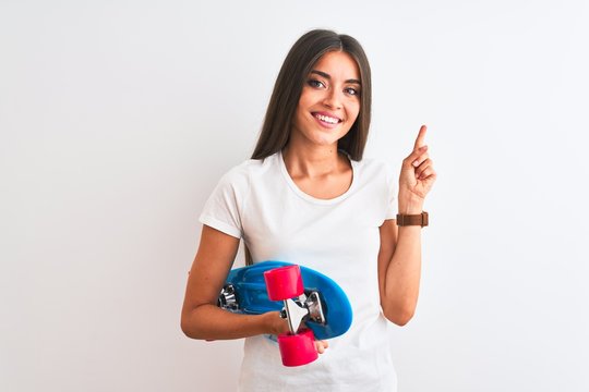 Young beautiful woman holding skate standing over isolated white background very happy pointing with hand and finger to the side