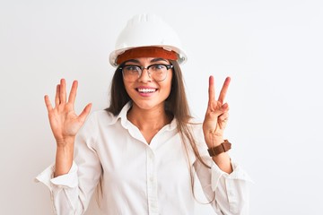 Young beautiful architect woman wearing helmet and glasses over isolated white background showing and pointing up with fingers number seven while smiling confident and happy.