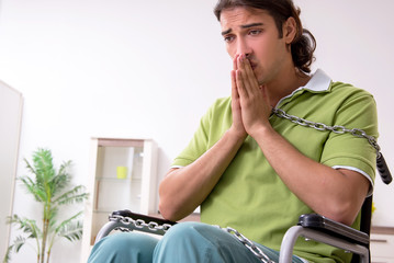 Young male invalid in wheel-chair suffering at home