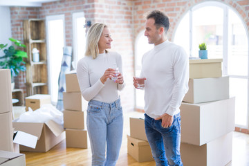 Fototapeta na wymiar Young beautiful couple standing drinking cup of coffee at new home around cardboard boxes