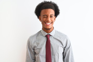 Young african american businessman wearing tie standing over isolated white background winking...