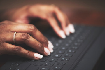 Isolated close-up of ethnic hands typing on black keyboard with white letters on wooden table