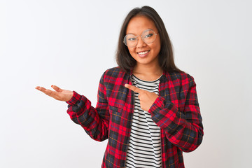 Young chinese woman wearing t-shirt jacket and glasses over isolated white background amazed and smiling to the camera while presenting with hand and pointing with finger.