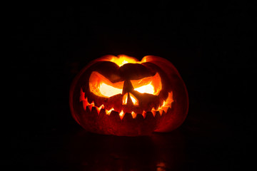 Close up view of scary Halloween pumpkin with eyes glowing inside at black background. Selective focus