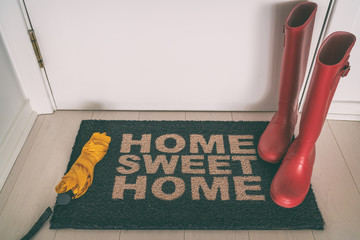 Autumn rain boots on entrance door mat at front of house with wet umbrella welcome rug on wooden...