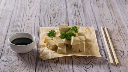 Soy sauce with slices of tofu cheese on paper with parsley. Soy cheese.