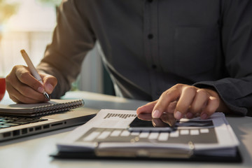 Businessman laptop usage and use of smartphone for payment And taking notes at office.