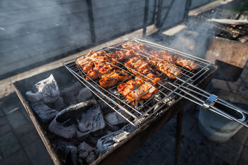 Close-up on the process of cooking shashlik of pork or beef meat clamped in a grill with a crispy burnt crust over gray burnt coals on an open fire with smoke going up.