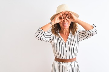 Obraz na płótnie Canvas Middle age businesswoman wearing striped dress and hat over isolated white background doing ok gesture like binoculars sticking tongue out, eyes looking through fingers. Crazy expression.