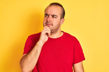 Young man wearing red casual t-shirt standing over isolated yellow background serious face thinking about question, very confused idea