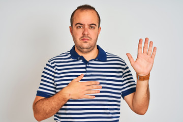 Young man wearing casual striped polo standing over isolated white background Swearing with hand on chest and open palm, making a loyalty promise oath