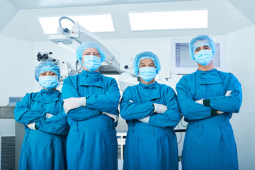 Positive confident proud surgeons in teal scrubs standing in operating room in front of medical...