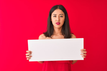 Young beautiful chinese woman holding banner standing over isolated red background with a confident expression on smart face thinking serious