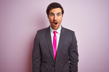 Young handsome businessman wearing suit and tie standing over isolated pink background afraid and shocked with surprise expression, fear and excited face.