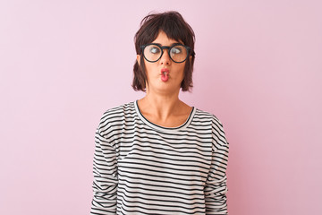 Young beautiful woman wearing striped t-shirt and glasses over isolated pink background making fish face with lips, crazy and comical gesture. Funny expression.