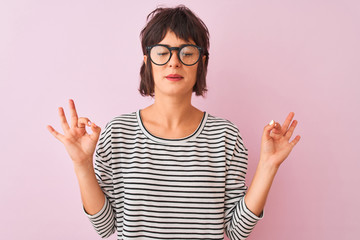 Young beautiful woman wearing striped t-shirt and glasses over isolated pink background relax and smiling with eyes closed doing meditation gesture with fingers. Yoga concept.