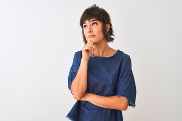 Young beautiful woman wearing denim dress standing over isolated white background with hand on chin thinking about question, pensive expression. Smiling with thoughtful face. Doubt concept.