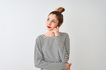 Redhead woman wearing navy striped t-shirt standing over isolated white background with hand on chin thinking about question, pensive expression. Smiling with thoughtful face. Doubt concept.