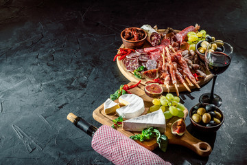Obraz na płótnie Canvas Antipasto platter with ham, prosciutto, salami, blue cheese, mozzarella, olives, grissini bread sticks with pesto and red wine on a dark background