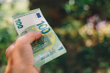 Male hand holding 100 hundredth euro banknote on green background