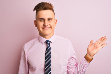 Young handsome businessman wearing shirt and tie standing over isolated pink background smiling cheerful presenting and pointing with palm of hand looking at the camera.