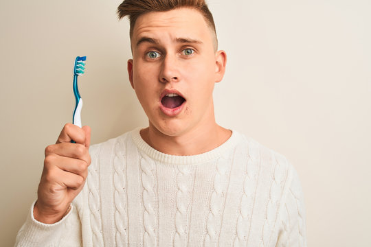 Young handsome man holding tooth brush standing over isolated white background scared in shock with a surprise face, afraid and excited with fear expression