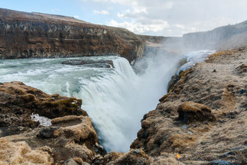 A three-step staircase of the Gullfoss waterfall on Hvita river, as pictured in detail (water plunging into the canyon, mossy cliffs, thick spray, panorama of the rapids)