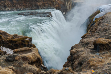 A three-step staircase of the Gullfoss waterfall on Hvita river, as pictured in detail (water plunging into the canyon, mossy cliffs, thick spray, panorama of the rapids)