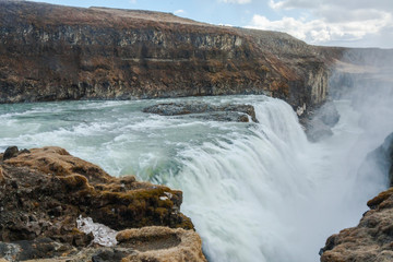 Fototapeta premium A three-step staircase of the Gullfoss waterfall on Hvita river, as pictured in detail (water plunging into the canyon, mossy cliffs, thick spray, panorama of the rapids)