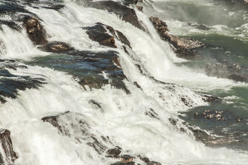 A three-step staircase of the Gullfoss waterfall on Hvita river, as pictured in detail (water plunging into the canyon, mossy cliffs, thick spray, panorama of the rapids)