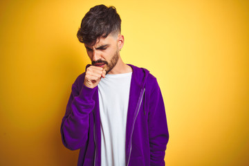 Young man with tattoo wearing sport purple sweatshirt over isolated yellow background feeling unwell and coughing as symptom for cold or bronchitis. Healthcare concept.