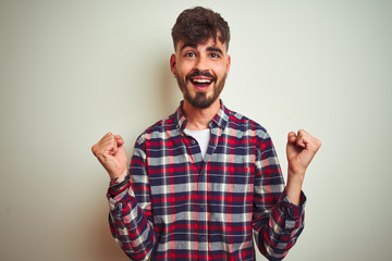 Fototapeta premium Young man wearing casual shirt standing over isolated white background celebrating surprised and amazed for success with arms raised and open eyes. Winner concept.