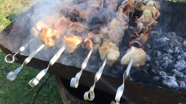 video footage with Chicken meat being grilled with heaton charcoals in barbeque with metal skewers with white smoke over them