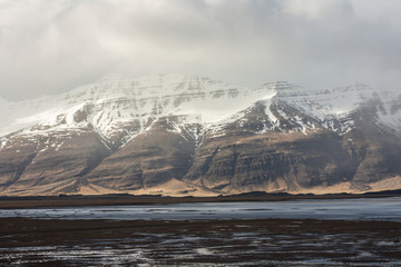 Obraz na płótnie Canvas Icelandic fjords in Eastern part of island as pictured with snowstorm clouds and snow covered mountain ranges in the background