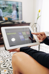 Close-up image of young woman using streaming media service application on tablet computer to choose movie, show or music on smart tv