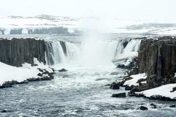 Fototapeta premium Selfoss waterfall (part of Jökulsá á Fjöllum river in the north of Iceland originating from Vatnajokull glacier) in winter, pictured with snow icicles, snow patterns and spray over the stream 