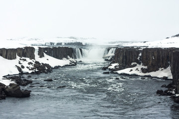 Selfoss waterfall (part of Jökulsá á Fjöllum river in the north of Iceland originating from Vatnajokull glacier) in winter, pictured with snow icicles, snow patterns and spray over the stream 