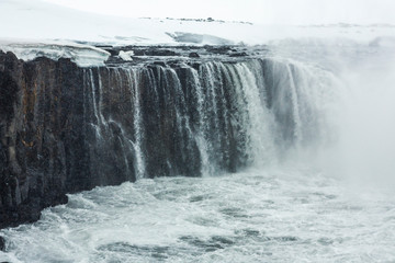 Fototapeta na wymiar Selfoss waterfall (part of Jökulsá á Fjöllum river in the north of Iceland originating from Vatnajokull glacier) in winter, pictured with snow icicles, snow patterns and spray over the stream 