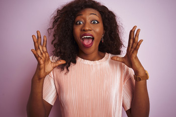 Young african american woman wearing t-shirt standing over isolated pink background celebrating crazy and amazed for success with arms raised and open eyes screaming excited. Winner concept