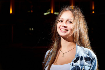 Portrait of young brunette woman with long hair on a city street at night and colored lights