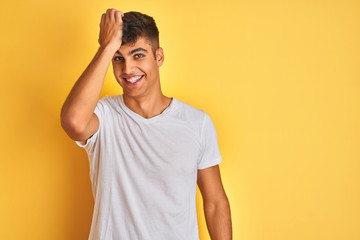 Young indian man wearing white t-shirt standing over isolated yellow background surprised with hand on head for mistake, remember error. Forgot, bad memory concept.