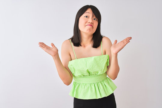 Young beautiful chinese woman wearing green t-shirt over isolated white background clueless and confused expression with arms and hands raised. Doubt concept.