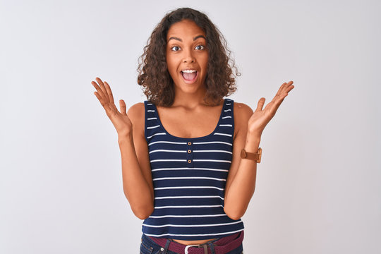 Young brazilian woman wearing striped t-shirt standing over isolated white background celebrating crazy and amazed for success with arms raised and open eyes screaming excited. Winner concept