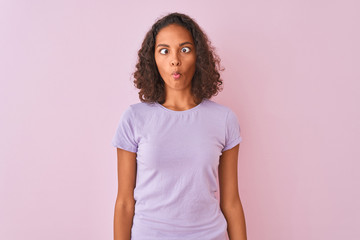 Young brazilian woman wearing t-shirt standing over isolated pink background making fish face with lips, crazy and comical gesture. Funny expression.