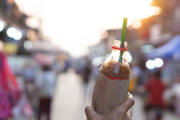 Closeup woman hand holding ice of cola flaver soda bottle on walking street, selective focus