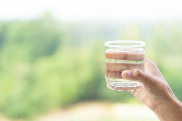 Close up woman hand holding a glass of pure water for dink with green nature background, Health...
