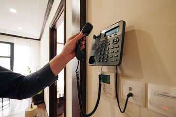 Cropped image of man using telephone in hotel room to order food and drinks or cleaning service