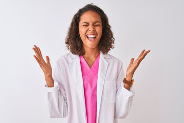 Young brazilian doctor woman wearing coat standing over isolated white background celebrating mad and crazy for success with arms raised and closed eyes screaming excited. Winner concept