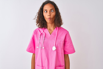 Young brazilian nurse woman wearing stethoscope standing over isolated white background making fish face with lips, crazy and comical gesture. Funny expression.