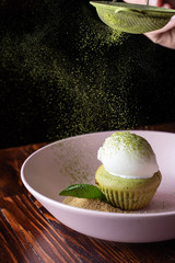 Male hand decorating matcha cupcake with a scoop of vanilla ice cream on wooden table